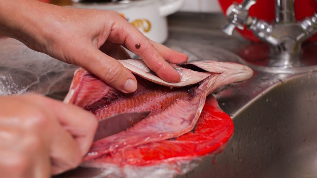 A person using a knife to slice open a fish.