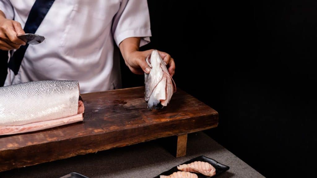 A chef holding the salmon head after slicing it off from the body